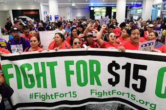 caption: Airport employees, Uber and Lyft drivers, and other workers protest for a $15 minimum wage at Los Angeles International Airport in October. Increases in minimum wages contributed to bigger pay gains for lower-income workers.