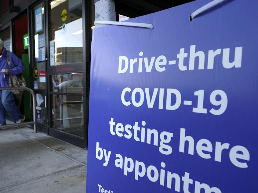 caption: A passer-by walks past a sign that calls attention to COVID-19 testing while departing a Walgreens pharmacy, Wednesday, Dec. 15, 2021, in New Bedford, Mass. (AP Photo/Steven Senne)