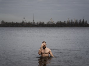caption: Nikolai Pastuchenko crosses himself as he takes a dip into the Dnipro River in Dnipro, Ukraine, on Thursday.