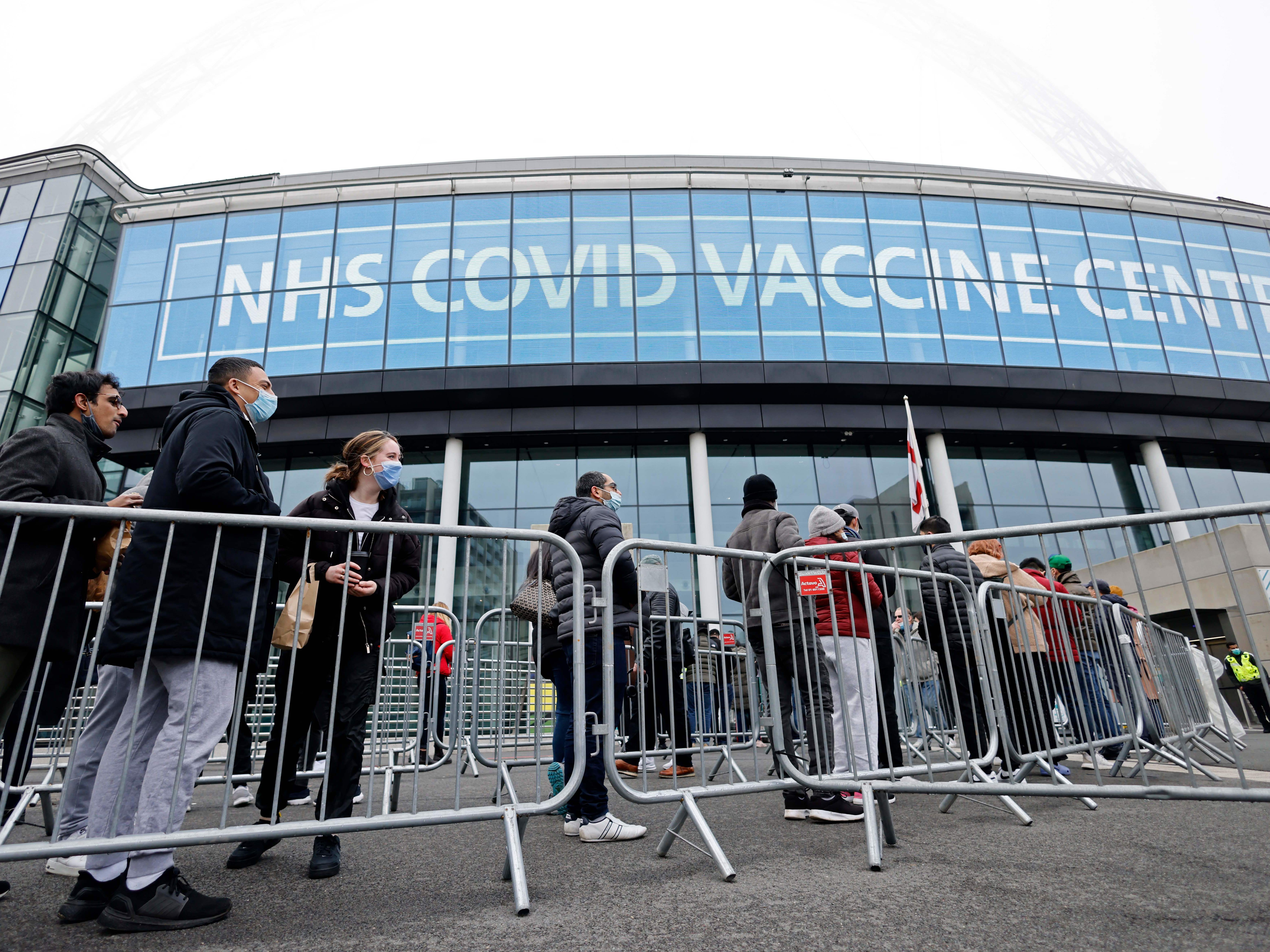 caption: People queue outside the newly set up Wembley Stadium vaccination center to receive their the COVID-19 vaccine or booster at a mass vaccination event in London on Sunday, as the booster rollout accelerates in England and case numbers spike.