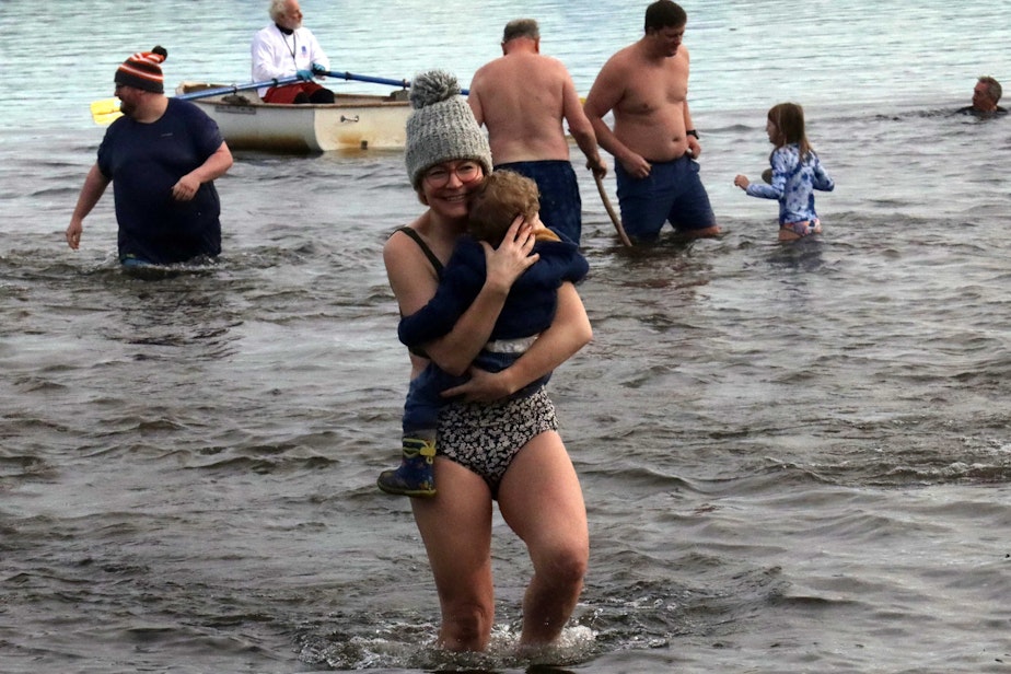caption: A mother and her child walk back to shore after taking a dip in Lake Washington during the Polar Bear Plunge on New Year's Day in Seattle.