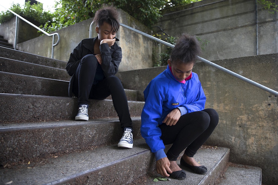 caption: Twin sisters Makalah, 12, left, and Akalah, right, sit on the steps at the Solid Ground Brettler Family Place, on Monday.