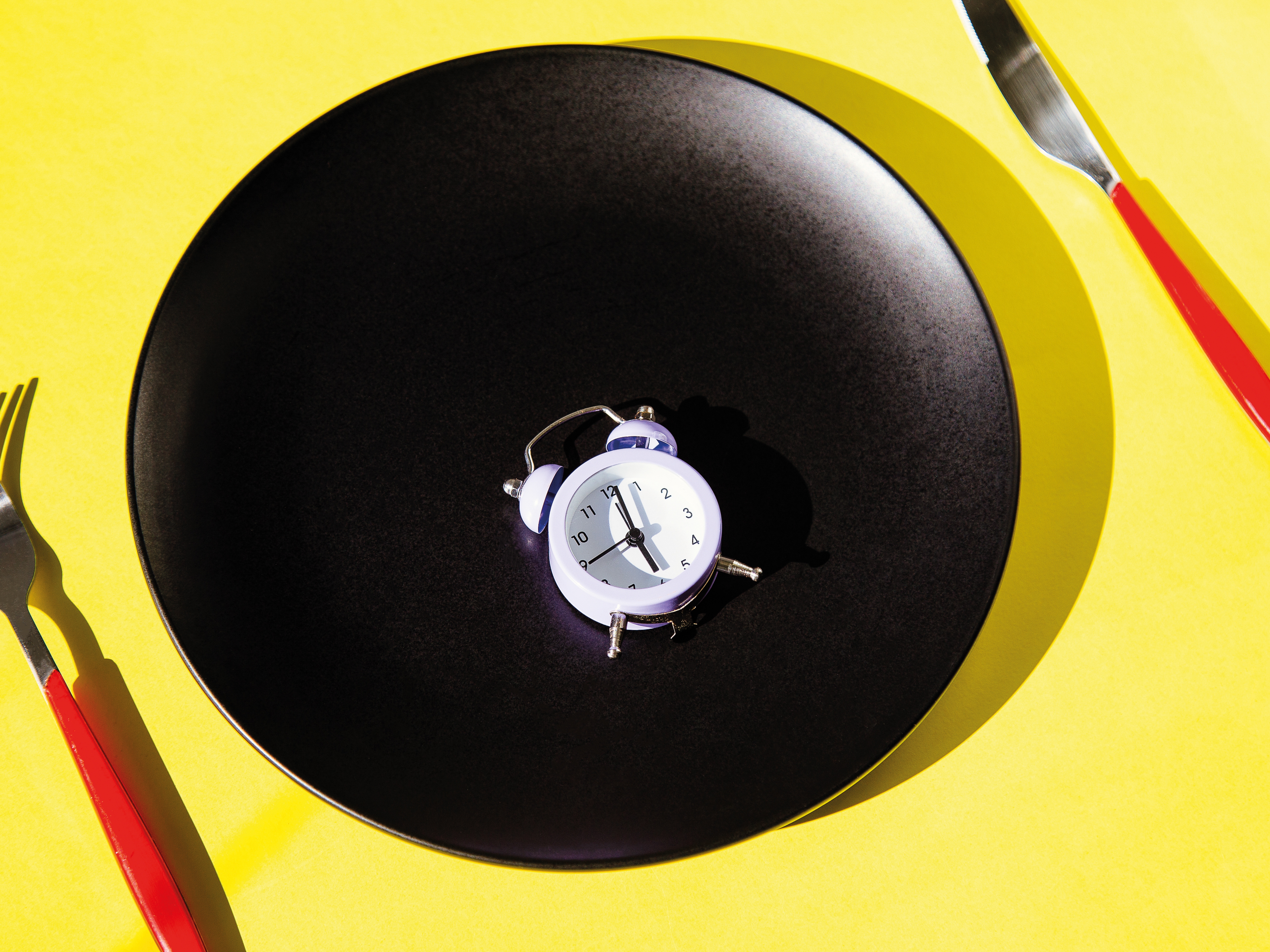 Clock alarm on the plate with cutlery on yellow background