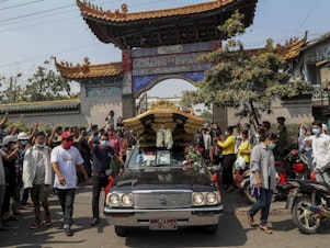 caption: Bystanders flash a three-fingered sign of resistance as the body of Kyal Sin leaves the Yunnan Chinese temple in Mandalay, Myanmar earlier this week.