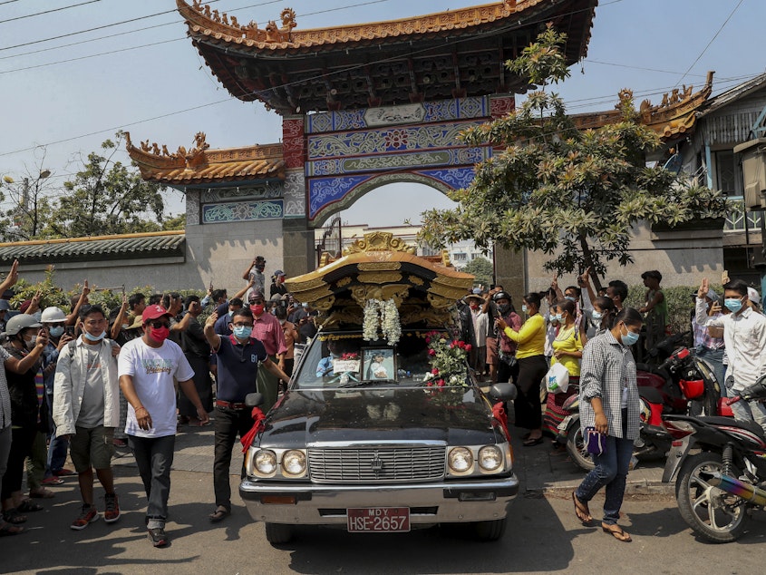 caption: Bystanders flash a three-fingered sign of resistance as the body of Kyal Sin leaves the Yunnan Chinese temple in Mandalay, Myanmar earlier this week.