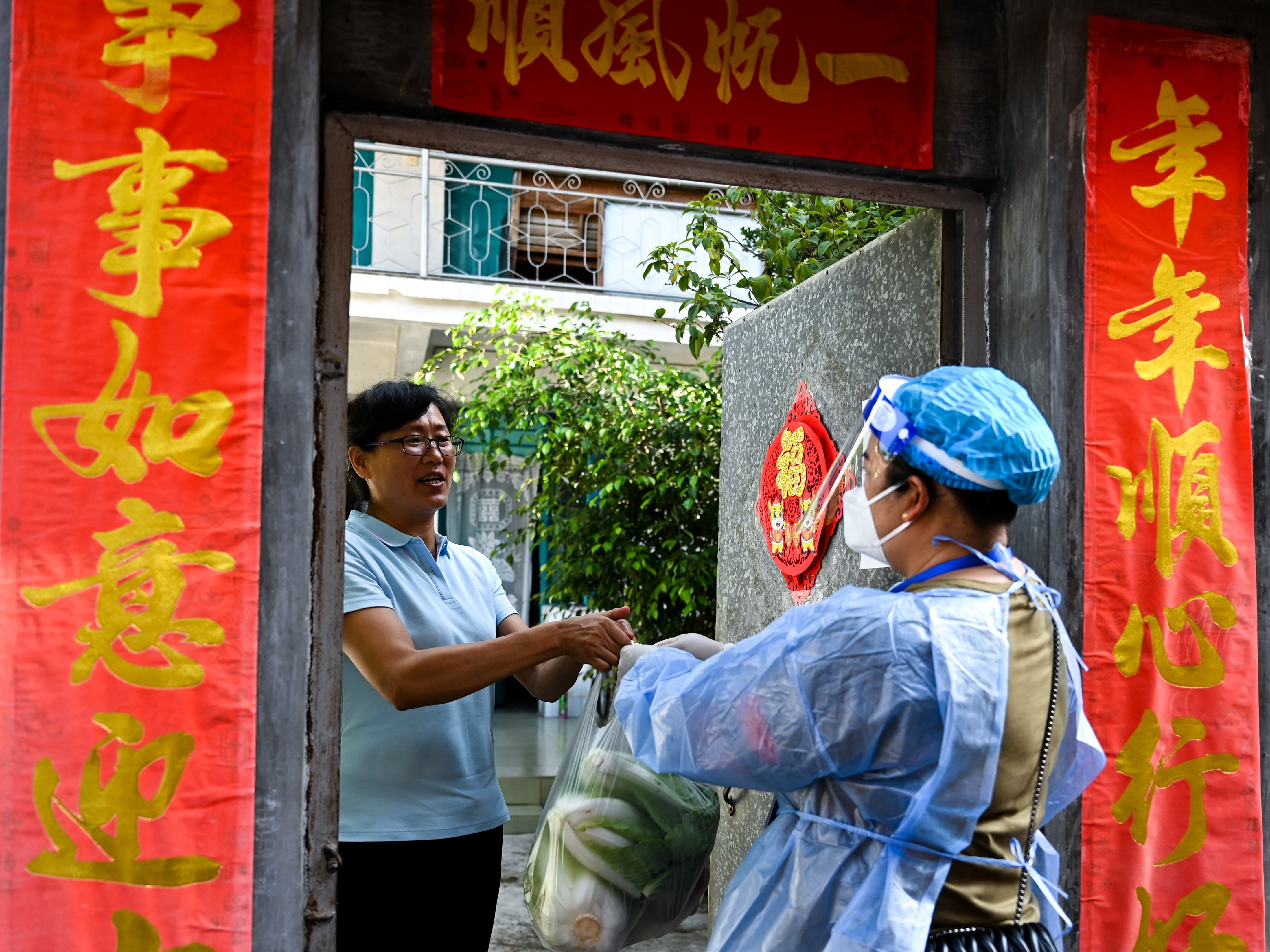 caption: A community worker delivered daily necessities to a household in Ruili City in China's Yunnan Province during a July lockdown triggered by COVID cases. Ruili closed off its city proper and asked all residents to quarantine at home. Classes were suspended. Most establishments were closed with the exception of markets, hospitals and pharmacies. Restaurants could only offer takeout food.