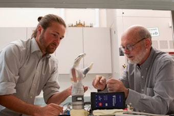 caption: University of Utah doctoral student Jacob George, left, and associate professor Greg Clark examine the LUKE Arm that they use for their experiments. A man who lost his lower arm in an electrical accident was able to experience some sense of touch and fine motor control with his grip while using the experimental device.