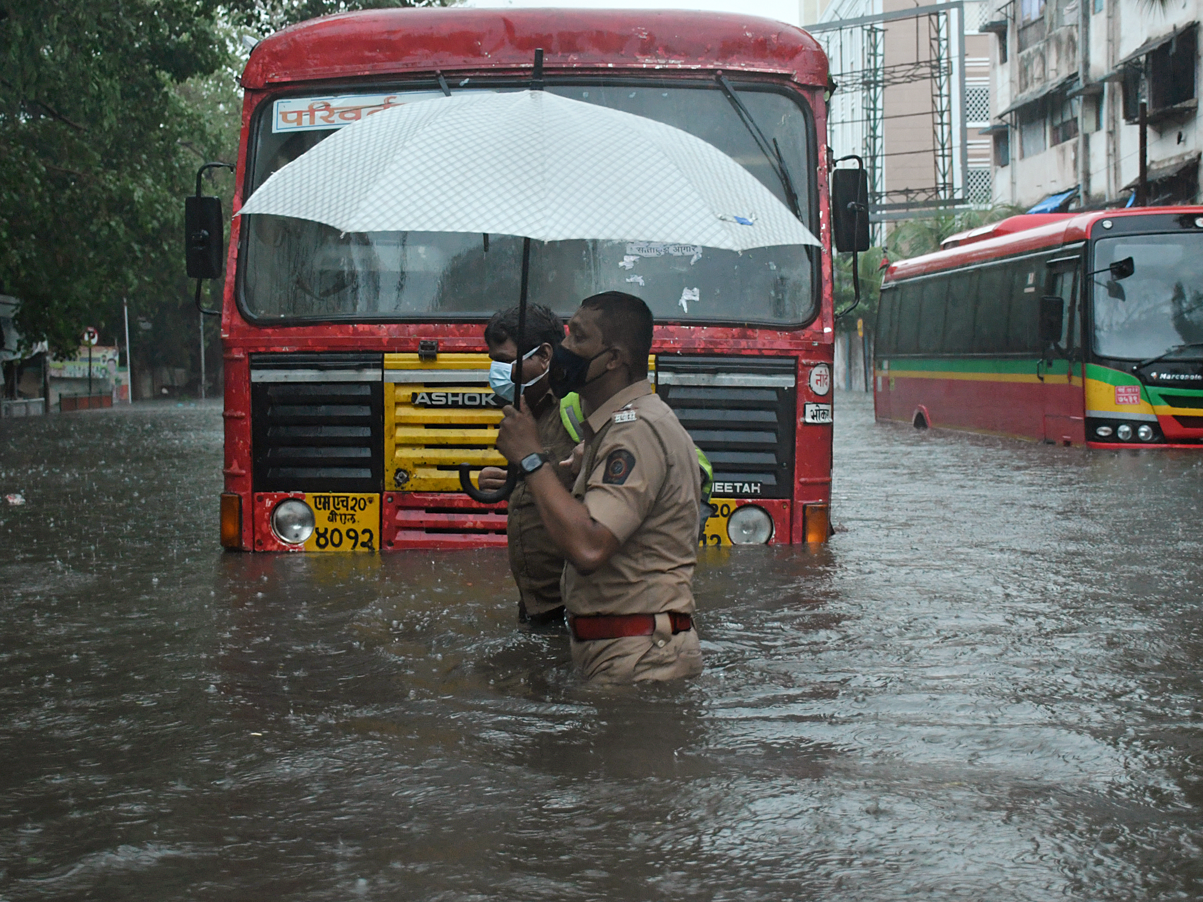 caption: A policeman helps a public transport driver to cross a flooded street due to heavy rain caused by cyclone Tauktae in Mumbai.