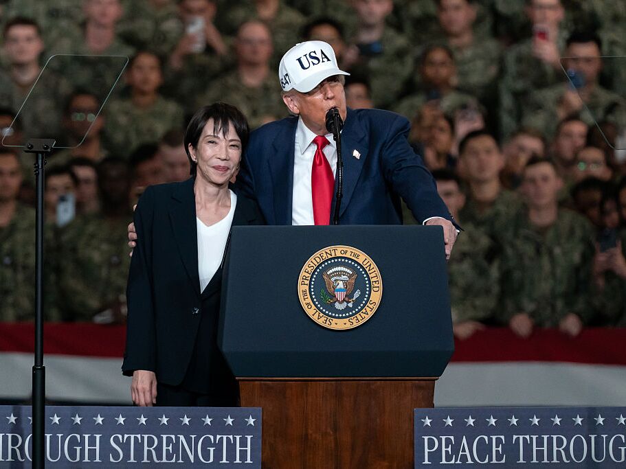 caption: Japanese Prime Minister Sanae Takaichi (R) listens as U.S. President Donald Trump (L) speaks to troops aboard USS George Washington on October 28, 2025 in Yokosuka, Japan.