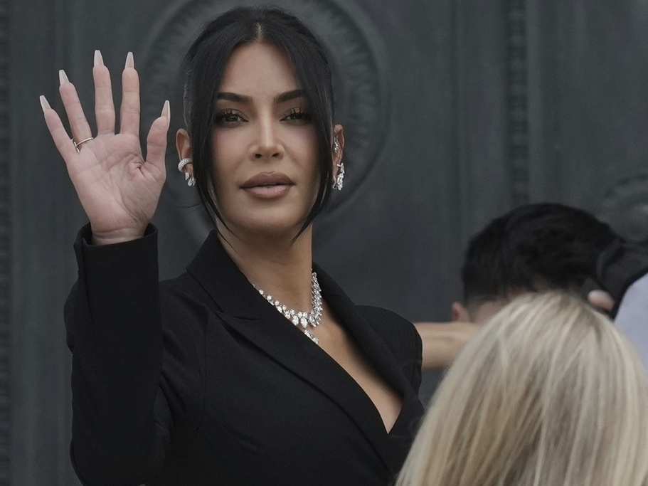 caption: Kim Kardashian waves as she arrives Tuesday to testify regarding a robbery of millions of dollars in jewels from her Paris hotel room in 2016.