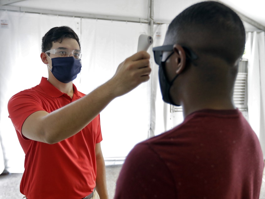 caption: Matt Comstock (left) takes the temperature of a guest at Busch Gardens in Tampa, Fla., on Wednesday. A spike in coronavirus cases in Florida and other states raised concerns in financial markets.