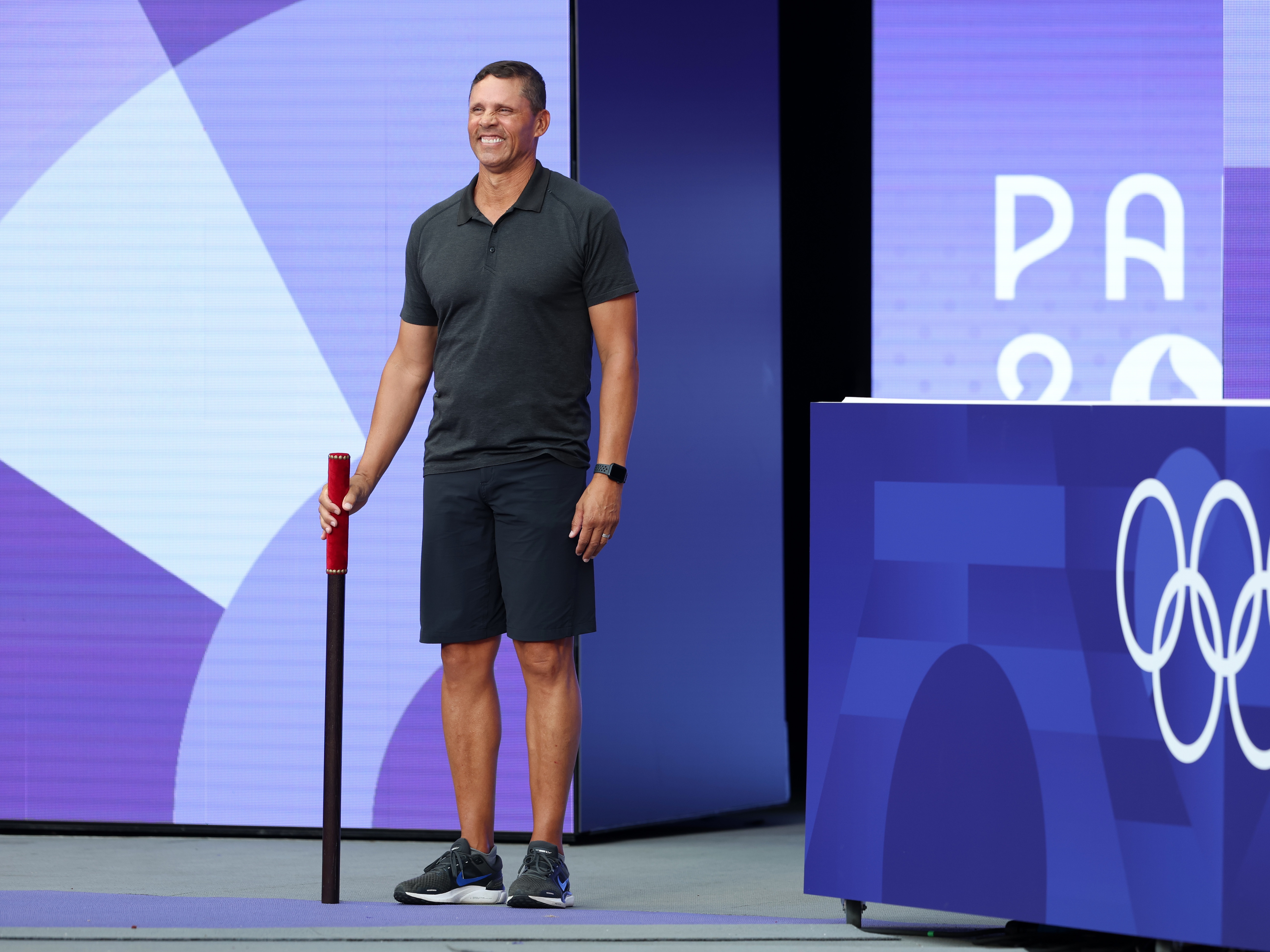 caption: Dan O'Brien, a former American decathlete, bears the brigadier ahead of the High Jump portion of the Decathlon at Stade de France on Friday. He's about to command the attention of the stadium's raucous crowd as part of a new, very French Olympic custom.