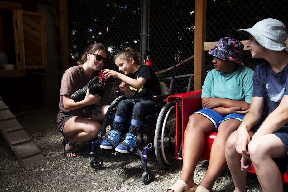 caption: Counselor Skye Anderson, left, and camper Madeline McCullough, second from left, interact with one of the camp's many chickens in the chicken coop, on Wednesday, July 16, 2025, at the Seattle PlayGarden.