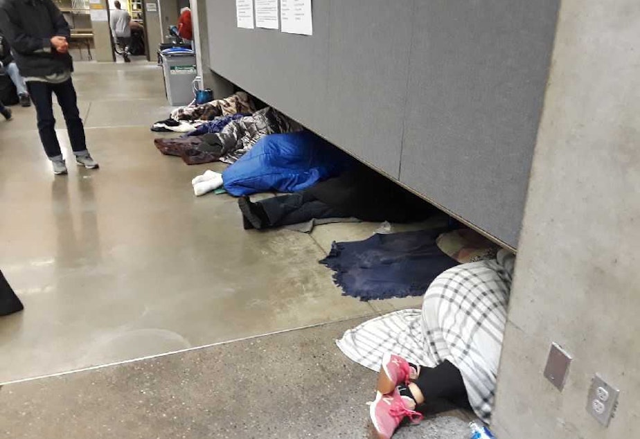 caption: People sleep while waiting in line early Thursday at the Seattle Center's Fisher Pavilion for a free health clinic to open.