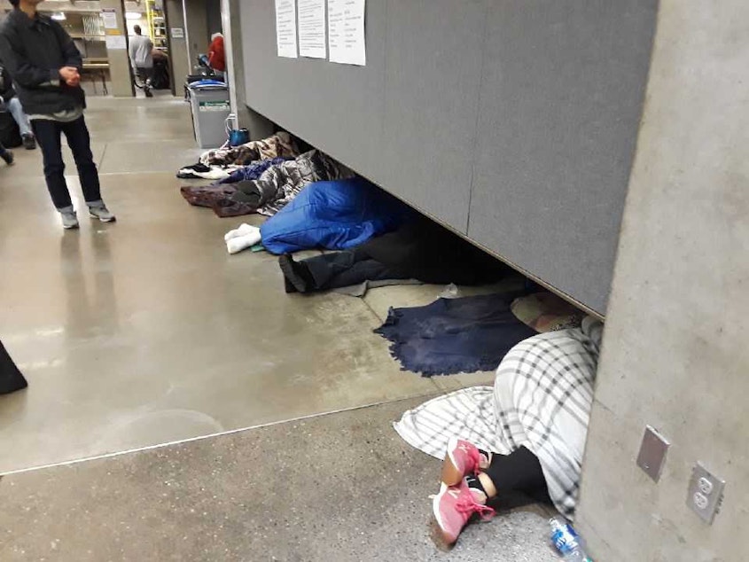 caption: People sleep while waiting in line early Thursday at the Seattle Center's Fisher Pavilion for a free health clinic to open.