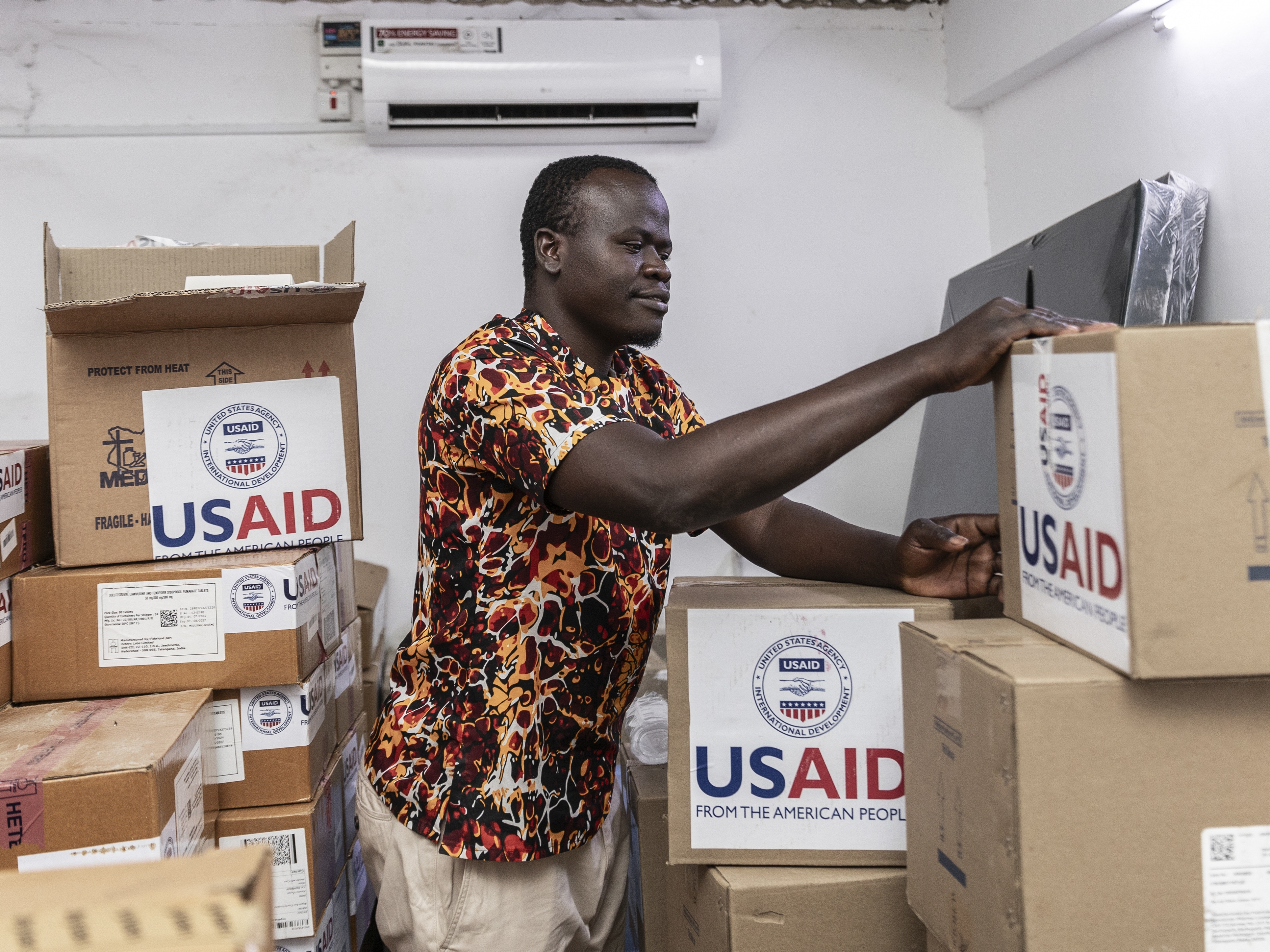 caption: On April 24, Kenyan pharmacist Joseph Njer Airo inspects boxes of antiretroviral drugs labeled "USAID," from the last donation before the funding cuts.