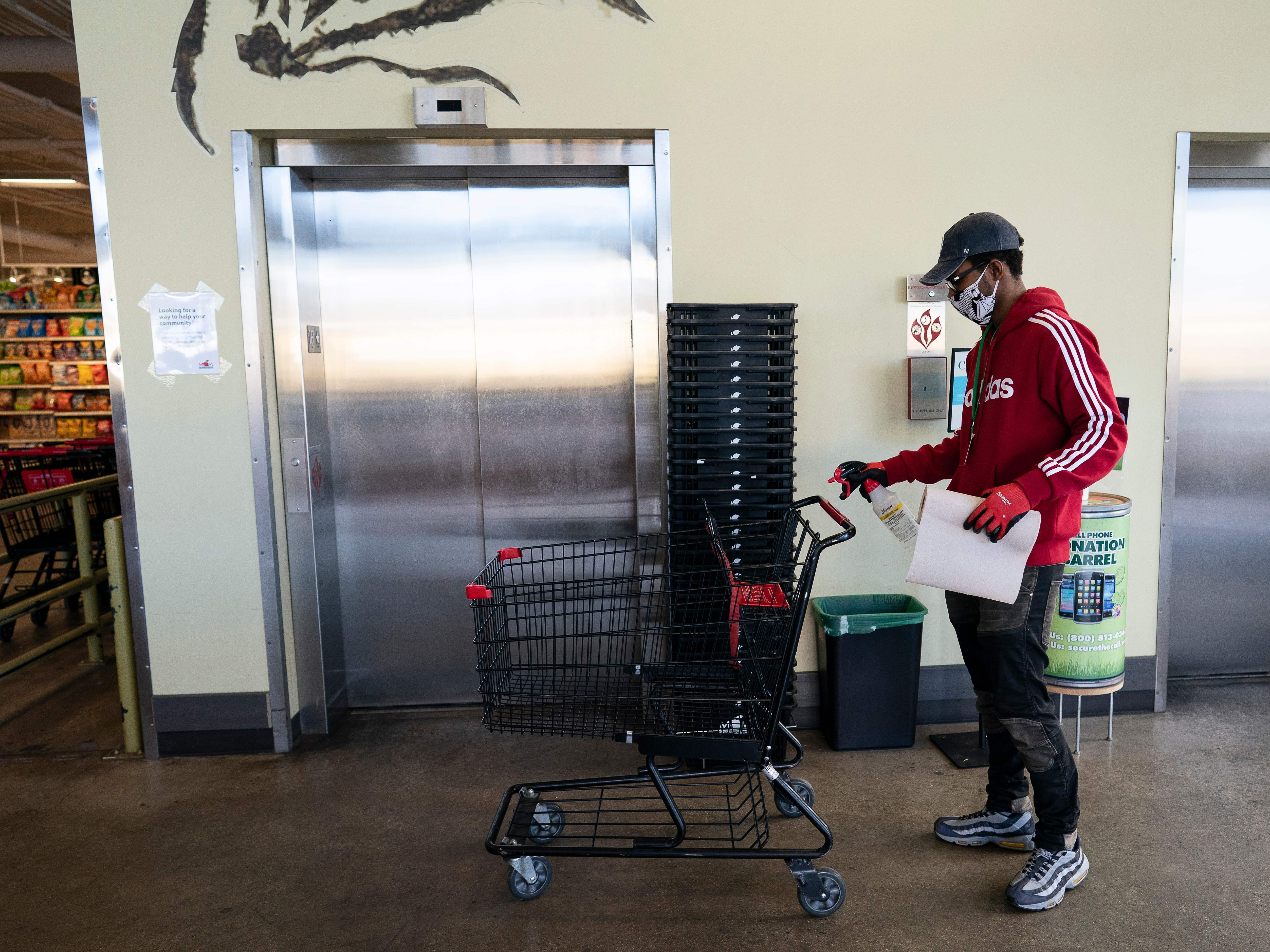 caption: A grocery store worker sanitizes a shopping cart at a MOM's Organic Market in Washington, D.C. in April 2020.