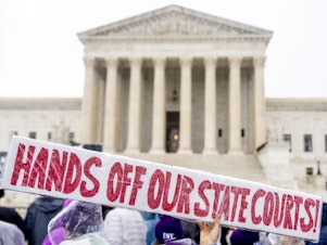caption: A demonstrator holds up a sign that reads "HANDS OFF OUR STATE COURTS!" during a December 2022 rally in front of the U.S. Supreme Court in Washington, D.C.