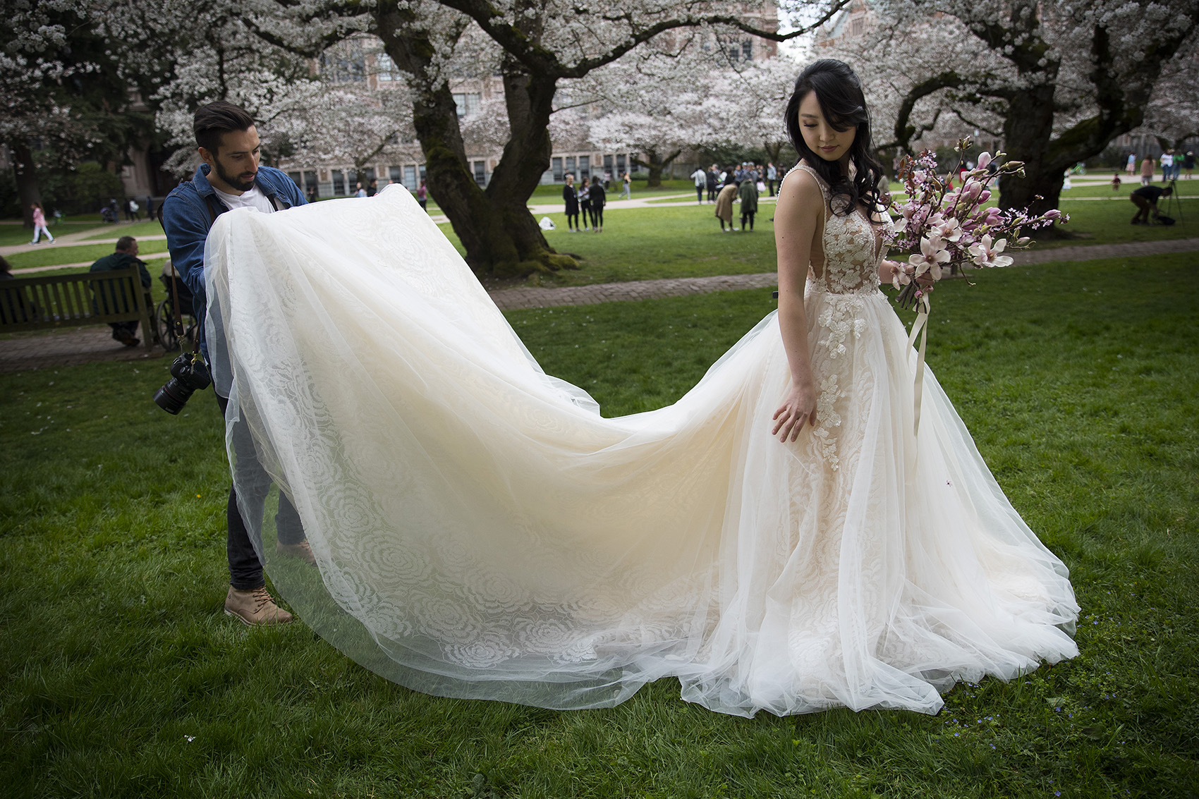 caption: Wedding photographer Wiley Putnam, left, adjusts floral designer Jane Kang's dress during a photo shoot for Juniper Rose Studio on Wednesday, March 27, 2019, on the University of Washington campus in Seattle.