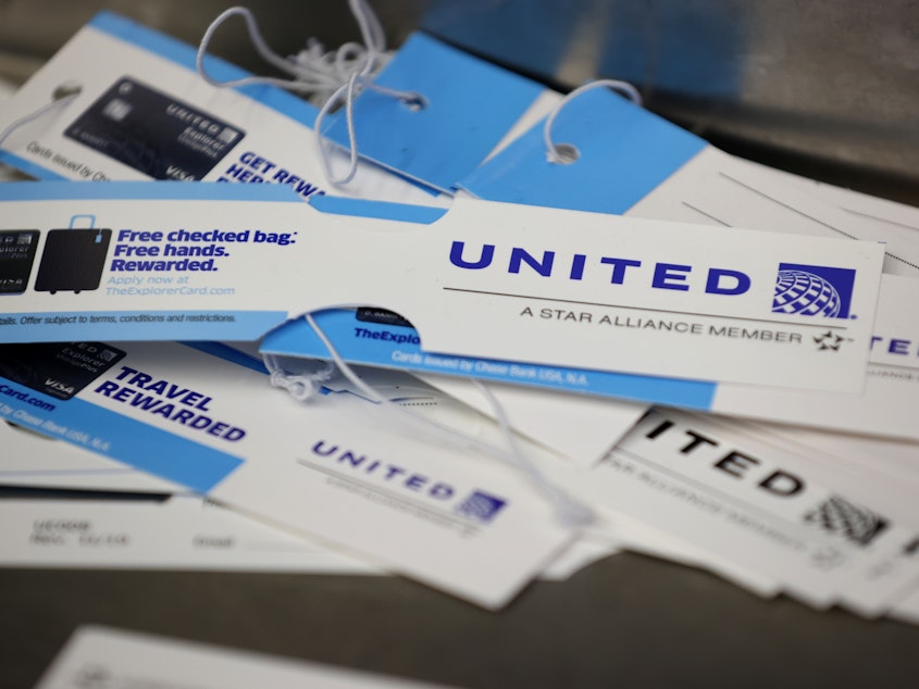 caption: United Airlines baggage tags are displayed on a table at San Francisco International Airport. The carrier says it's starting a pilot program next month that will offer rapid coronavirus testing at the airport or via a self-collected, mail-in test ahead of a flight.