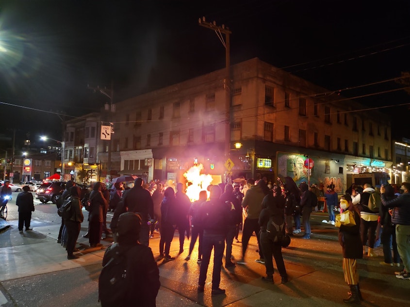 caption: A group of anti-fascist people protesting both Trump and Biden started a dumpster fire at the intersection of 10th and Pike on Capitol Hill Saturday night. 