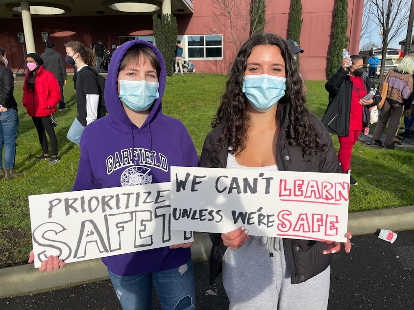 caption: Jacqueline Miller (right) and Rebecca McCann (left) hold signs calling on Seattle Public Schools to prioritize safety during a surge of omicron cases within SPS.