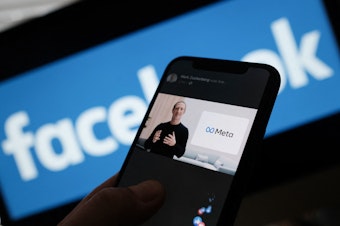 caption: In this illustration photo taken in Los Angeles on Oct. 28, 2021, a person watches on a smartphone as Facebook CEO Mark Zuckerberg unveils the META logo. The name of Facebook's parent company was changed to Meta to represent a future beyond just its troubled social network.