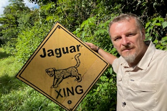caption: Chris Morgan with a sign warning about jaguars in the jungles of Belize. 