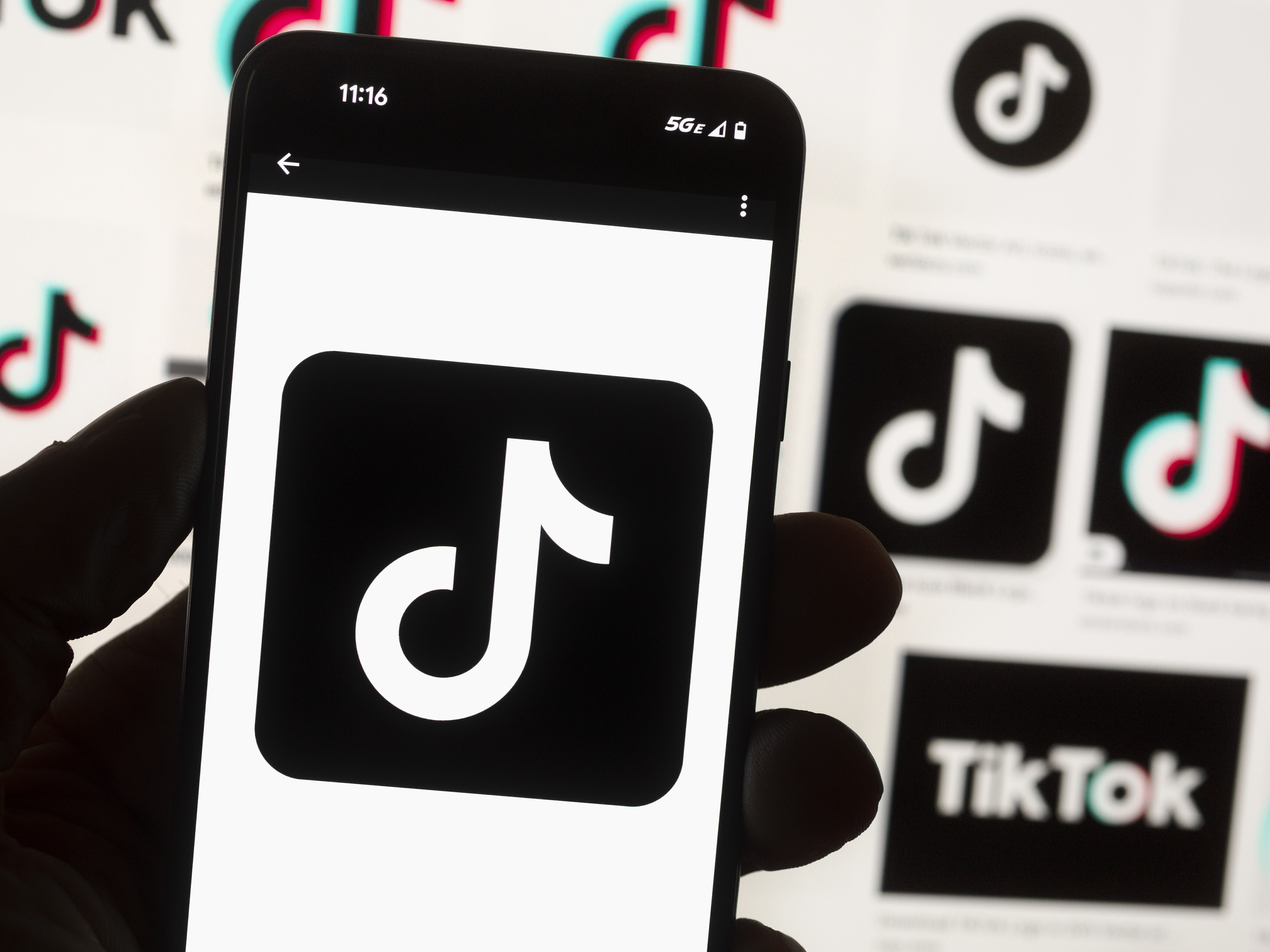 caption: The TikTok logo is seen on a mobile phone in front of a computer screen which displays the TikTok home screen, Oct. 14, 2022, in Boston.