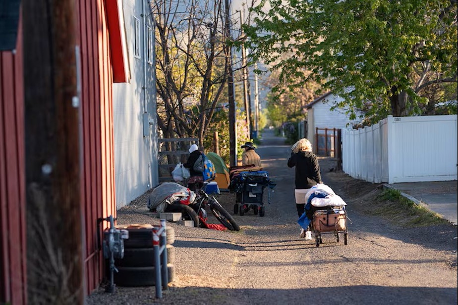 caption: Since camping and shelter restrictions were passed, Clarkston’s homeless encampment has dwindled from 75 people to about 20. Those who remain are forced to move their belongings, creating piles of supplies in an alleyway near Foster Park.