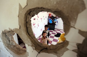 caption: Displaced Yemeni children stare through a hole in the wall of a half-destroyed house in Taez, where they have been staying with several families since violence drove them from their homes in Hodeidah earlier this year.