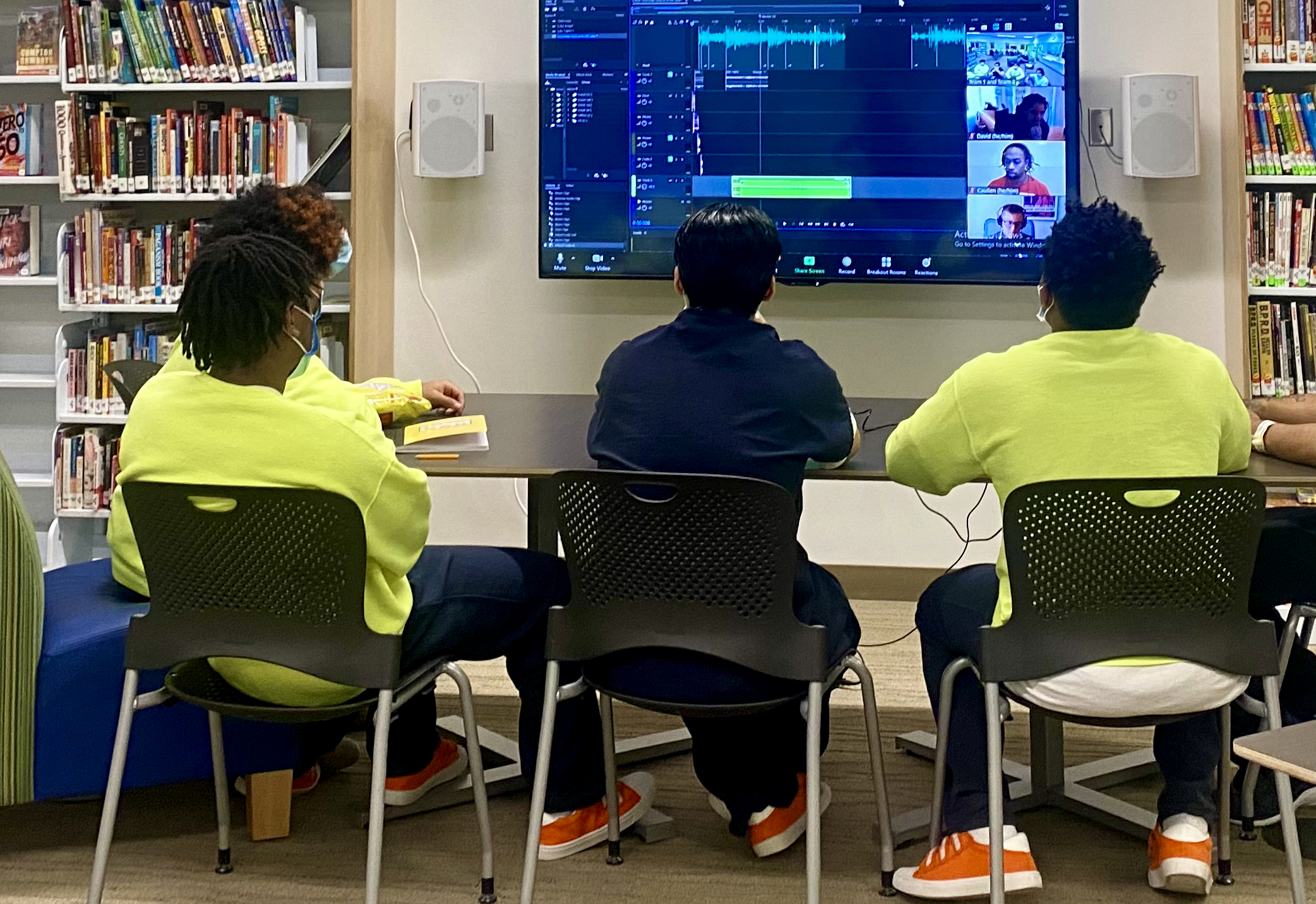 caption: Five youth sit around a table and listen as their audio stories play over a large computer screen on April 15, 2021.