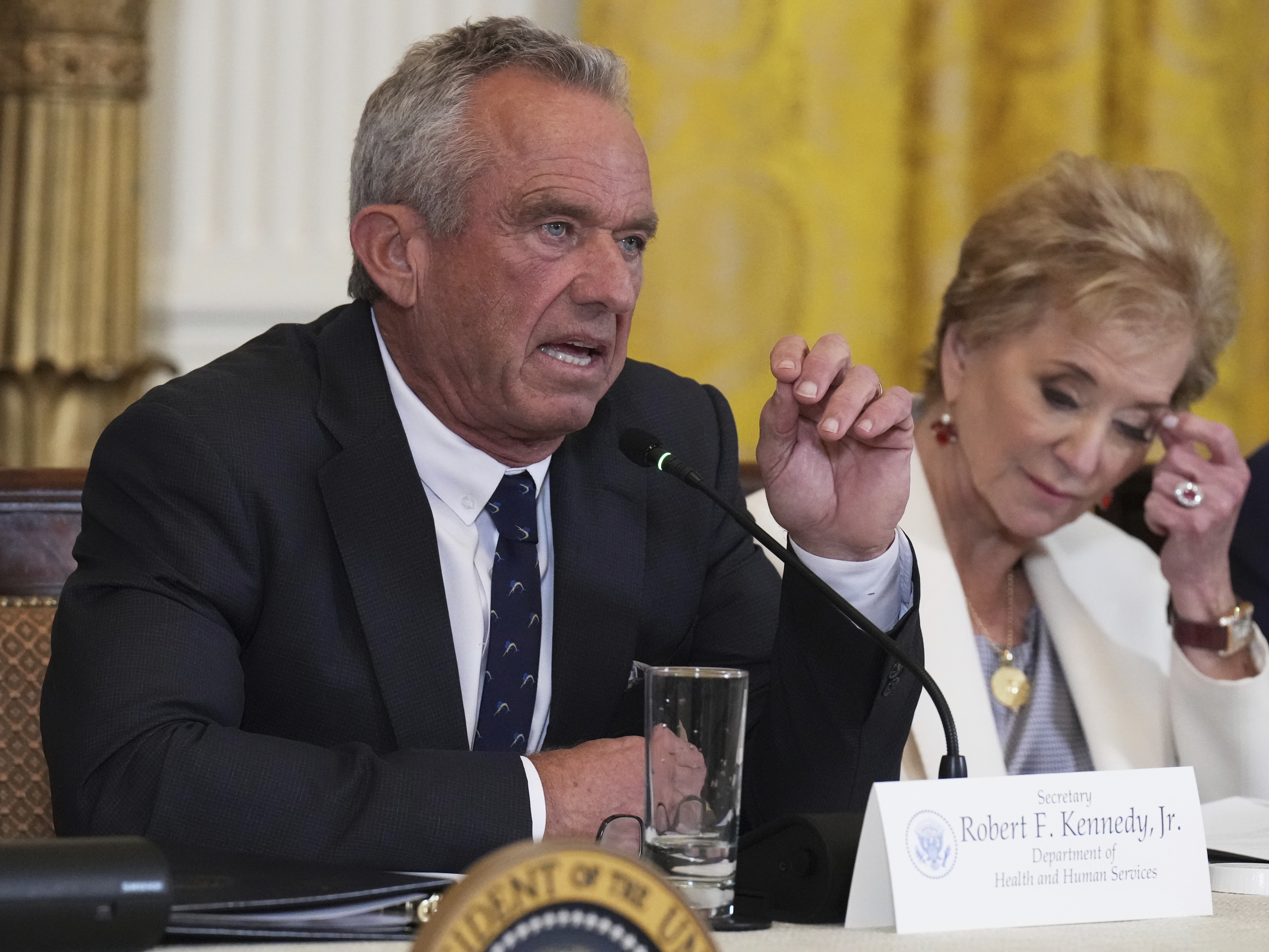 caption: Health and Human Services Secretary Robert F. Kennedy Jr. speaks as Education Secretary Linda McMahon listens during a Make America Healthy Again (MAHA) Commission Event in the East Room of the White House, Thursday, May 22, 2025, in Washington.
