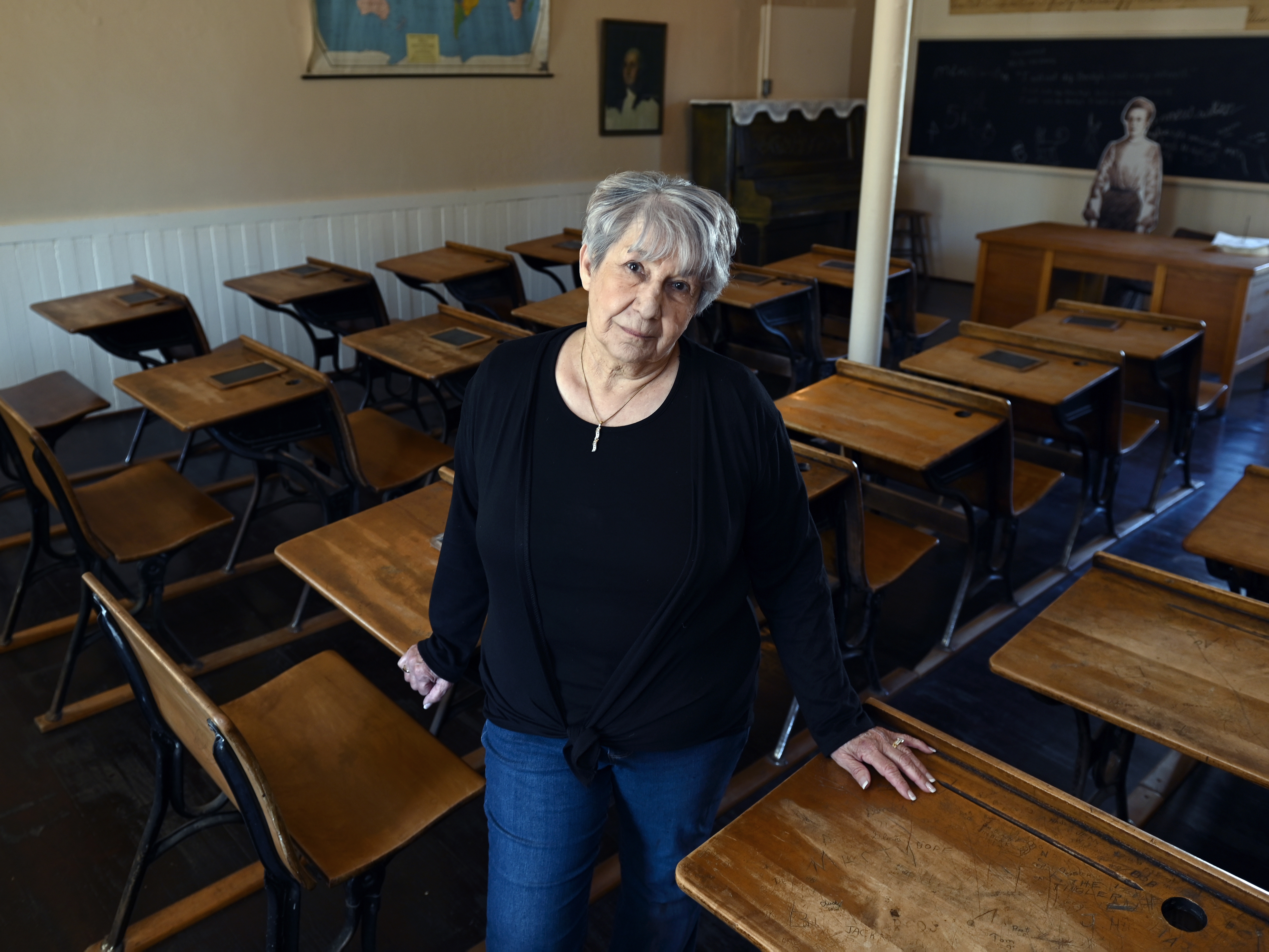 caption: Ramona Klein poses for a photo in a classroom at the former Fort Totten Indian Industrial School in North Dakota. Klein attended the boarding school from 1954 to 1958.