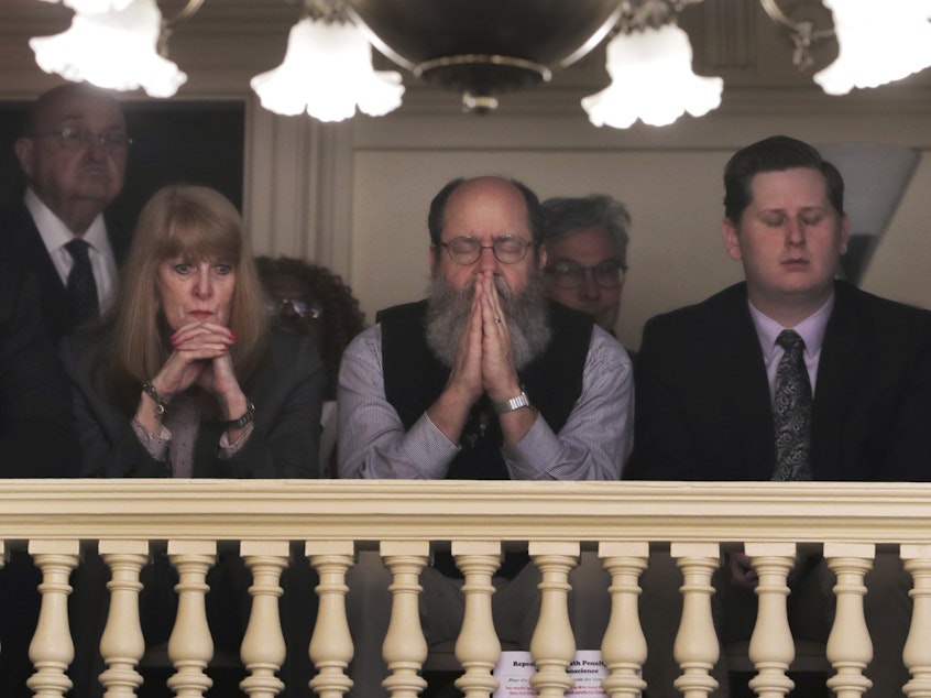 caption: Rob Spencer, center, prays as New Hampshire lawmakers debate prior to a death penalty vote at the State House in Concord, N.H., Thursday. The legislature abolished capital punishment by overriding a veto by Gov. Chris Sununu.