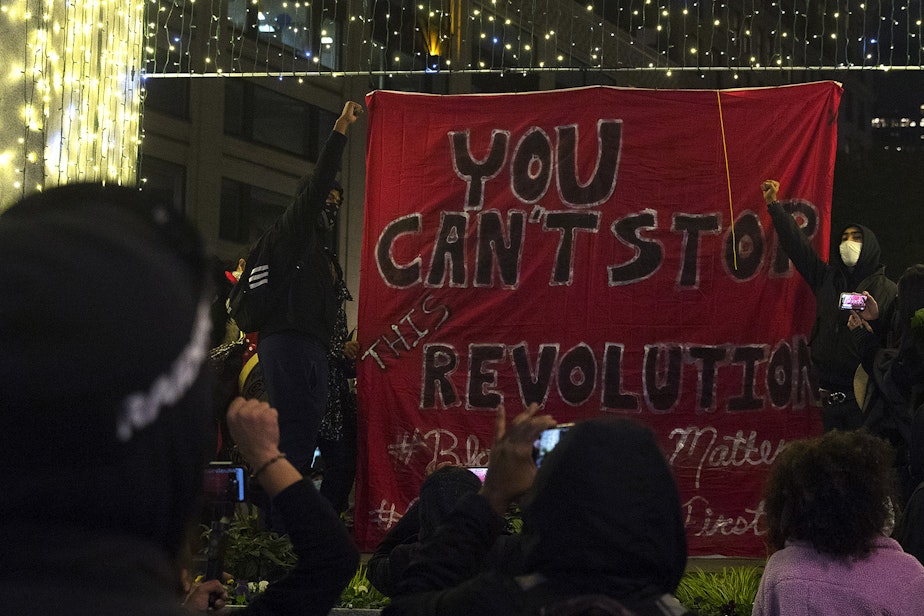 caption: Organizers raise their fists in the air after unfurling a banner reading, 'You can't stop this revolution,' on Monday, October 26, 2020, during the 150th day of protests for racial justice in Seattle at Westlake Park.