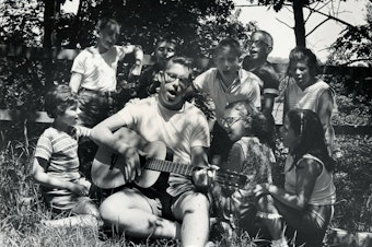 caption: A camp counselor plays the guitar and leads children in singing at Camp Butwin in Minnesota in 1962.