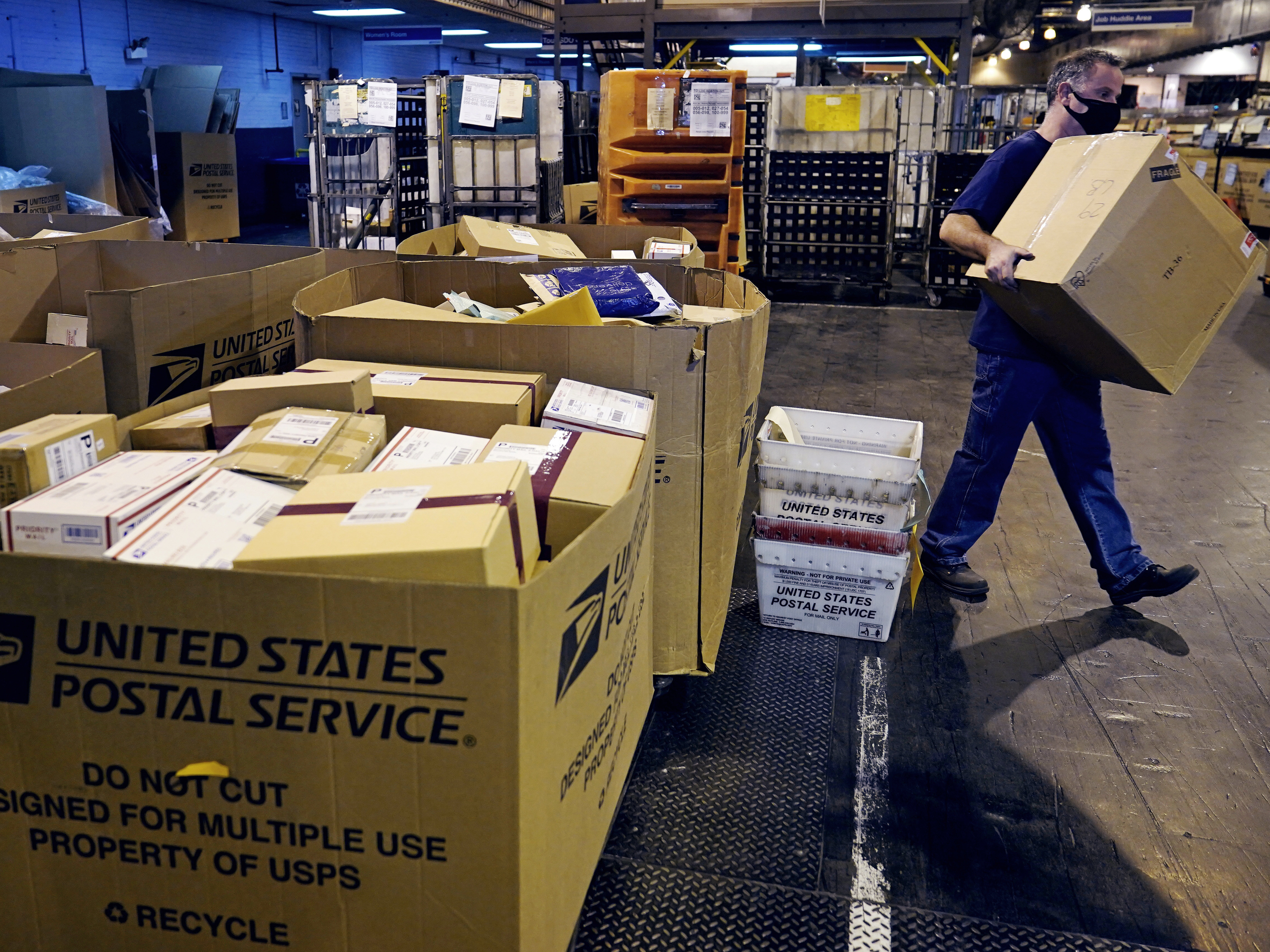 caption: A worker carries a large parcel at the United States Postal Service sorting and processing facility in Boston on Nov. 18, 2021.