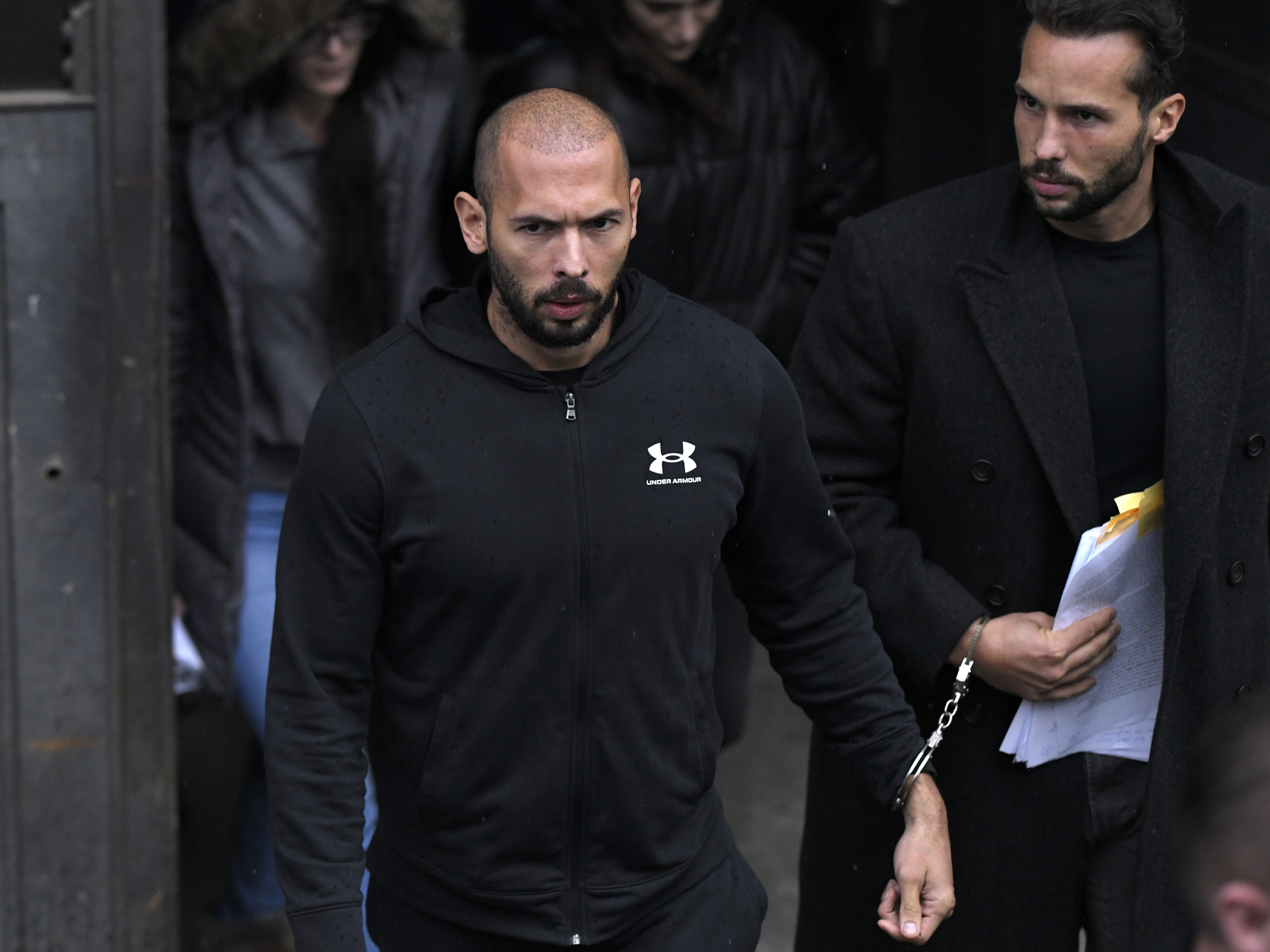 caption: Andrew Tate (center) and his brother Tristan leave after appearing at the Court of Appeal, in Bucharest, Romania, on Tuesday.