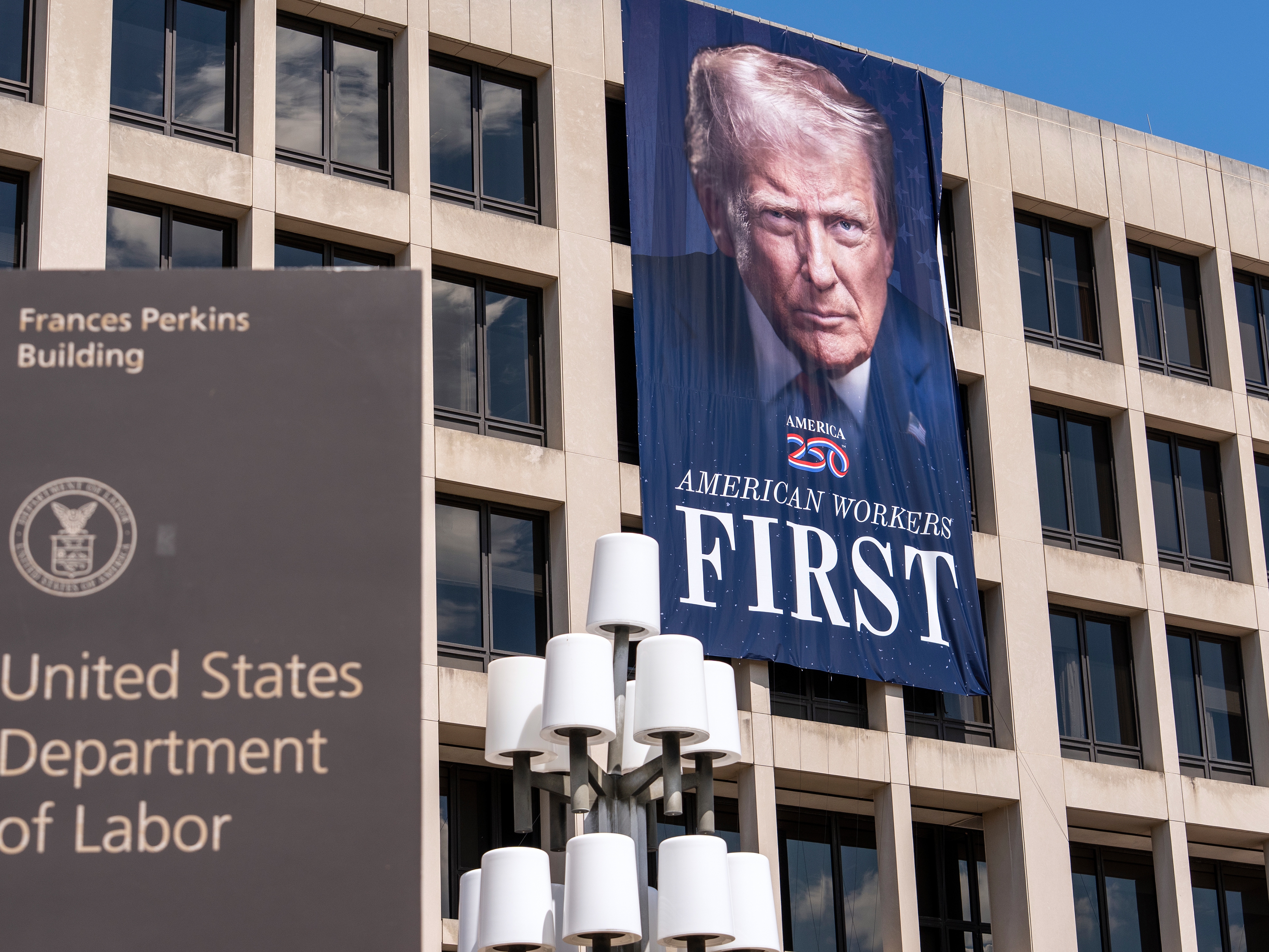 caption: A portrait of President Trump hangs on the Labor Department headquarters in Washington, D.C., on Aug. 25. The agency is bringing back some workers who took the government's deferred resignation offer. Still other employees whose jobs were eliminated received notices that they would be assigned to new positions.