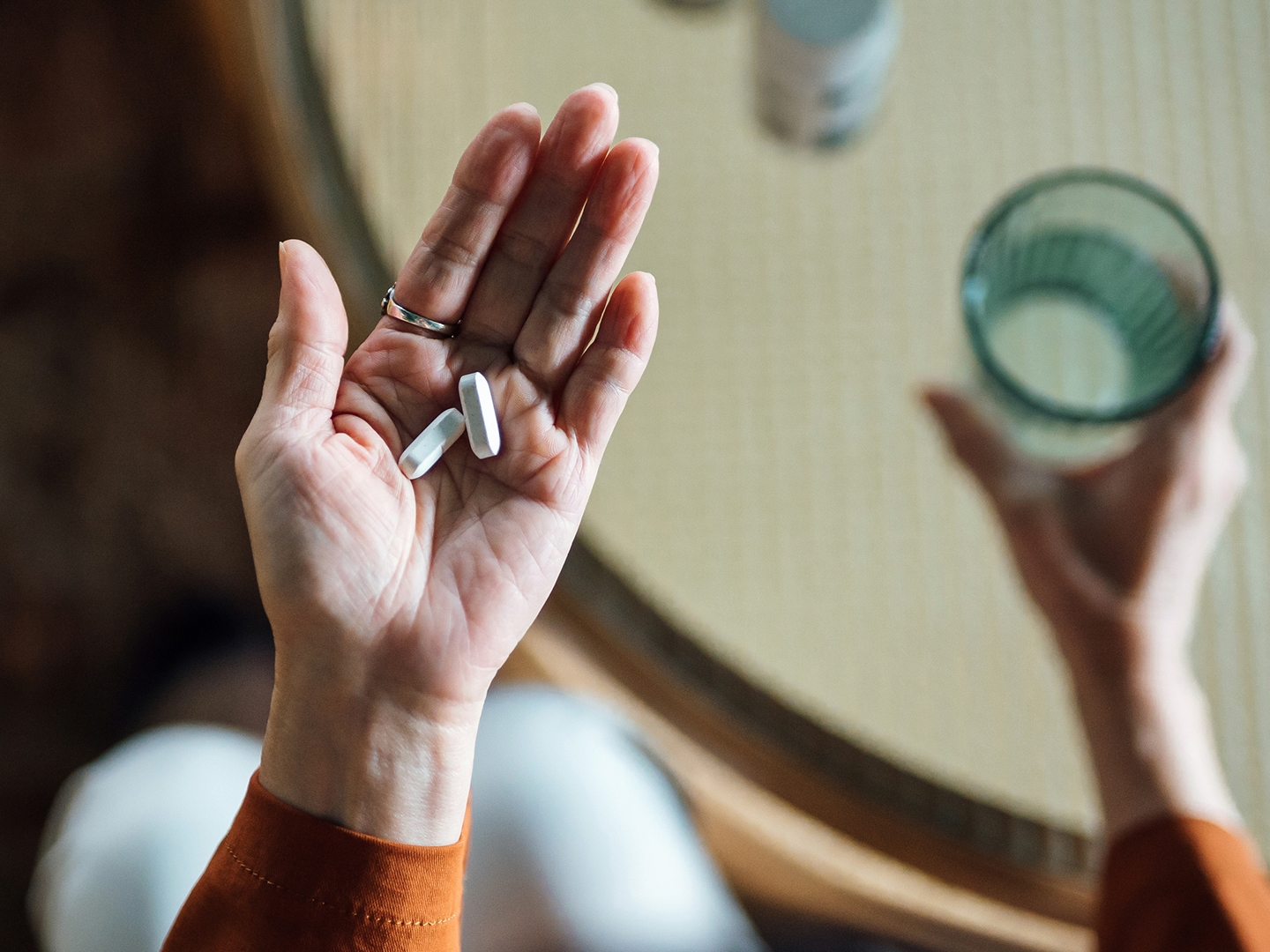 Overhead view of senior Asian woman feeling sick, taking medicines in hand with a glass of water at home. Elderly and healthcare concept
