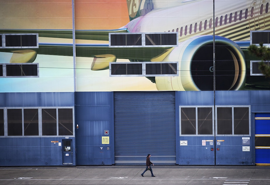 caption: A Boeing employee walks out of the Boeing Renton Factory after shift change on Monday, Dec. 16, 2019, in Renton.