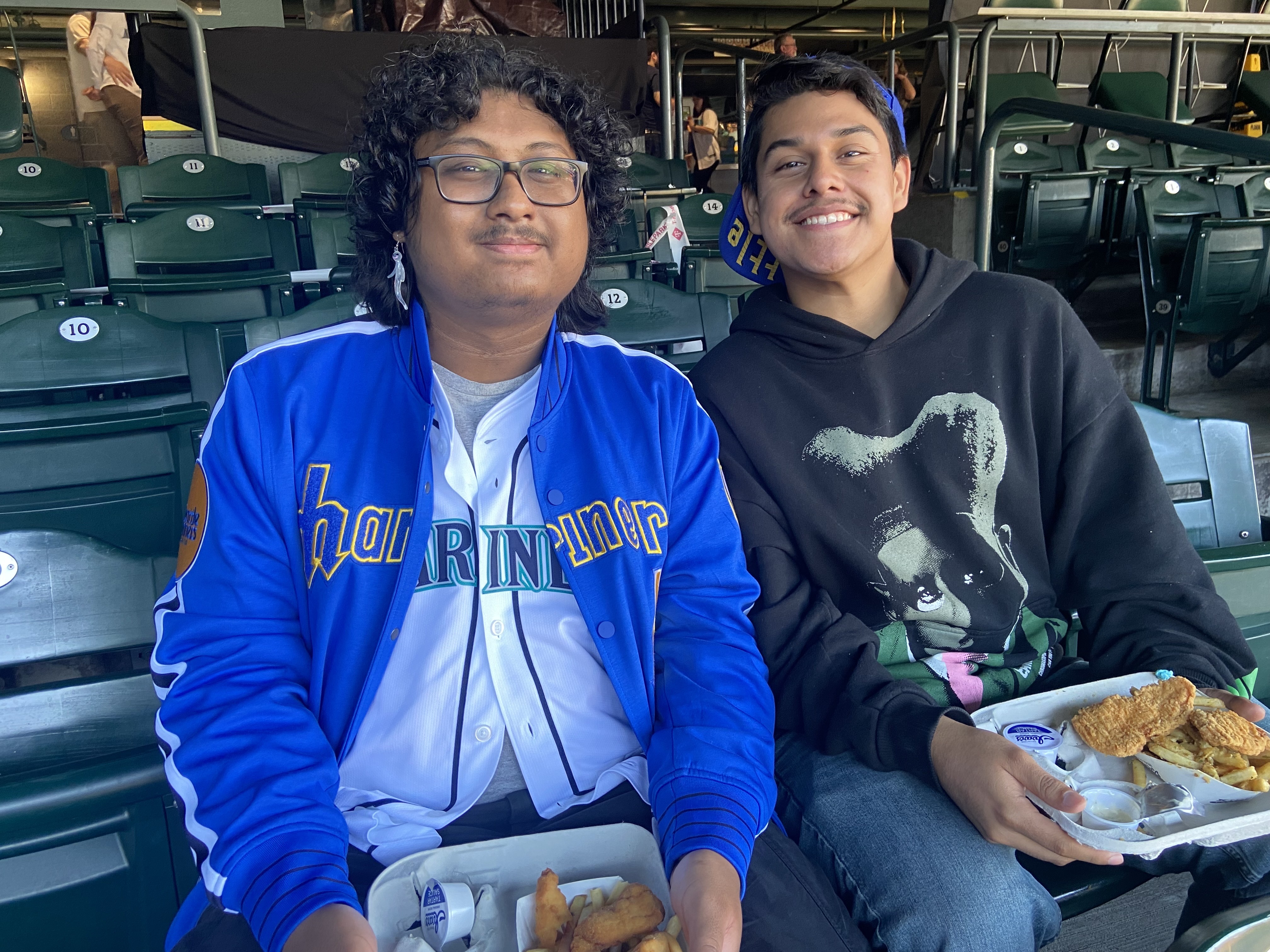 caption: Friends Sov Sot (left) and Alex Zelgado (right) snack while they wait for the Mariners to take on the Detroit Tigers in Game 3 of the American League Division Series.