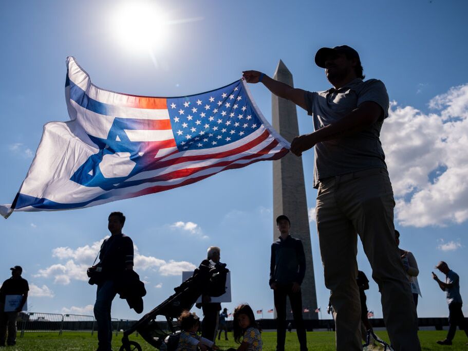 caption: An attendee holds a U.S. and Israeli flag at an October 7th memorial rally near the Washington Monument in Washington, D.C., on Oct. 7, 2024.