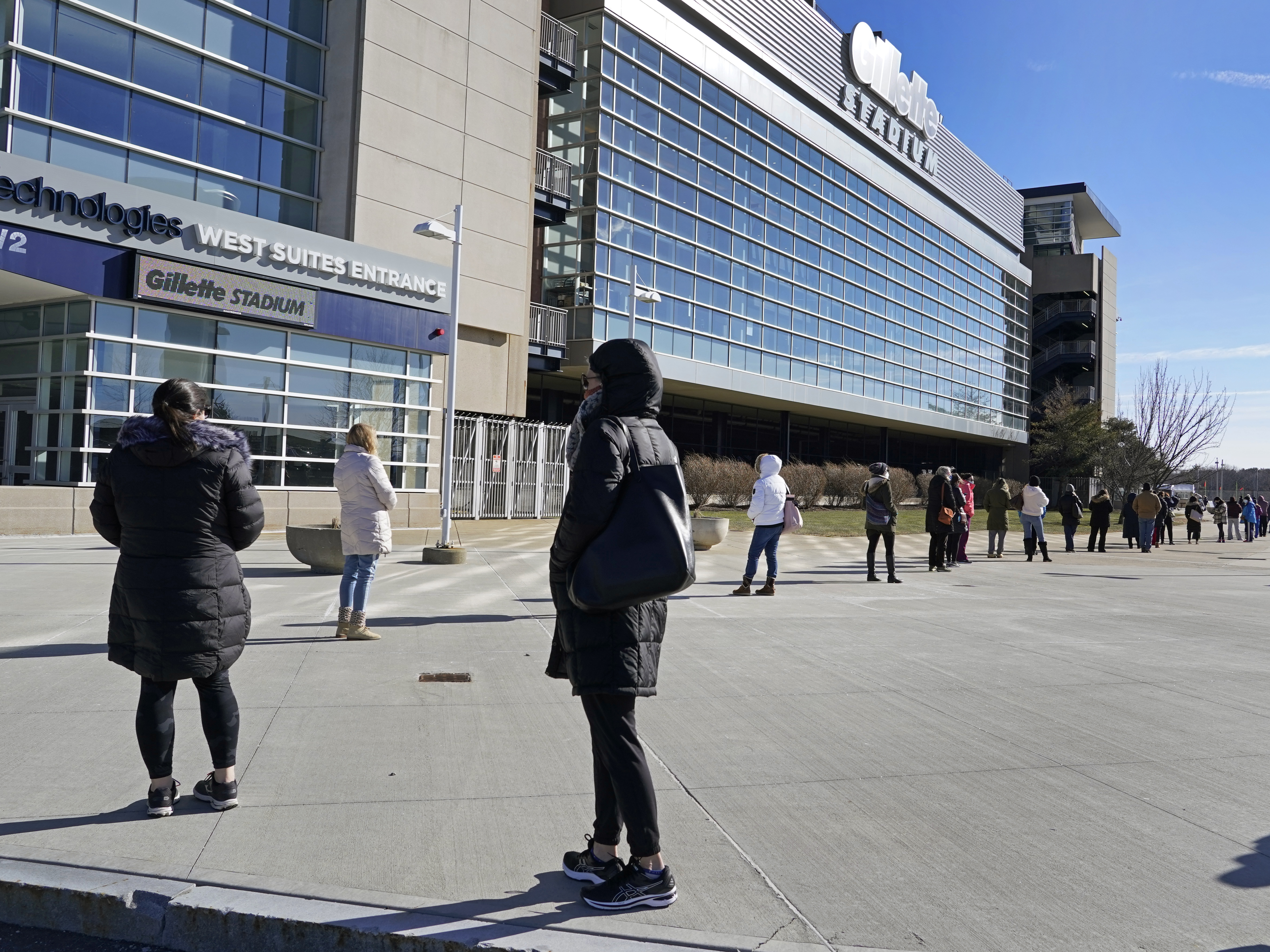 caption: People wait in a socially distanced line to get their COVID-19 vaccinations at Gillette Stadium in Foxborough, Mass., last month. The NFL is making all 30 of its stadiums available to serve as mass vaccination sites.