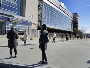 caption: People wait in a socially distanced line to get their COVID-19 vaccinations at Gillette Stadium in Foxborough, Mass., last month. The NFL is making all 30 of its stadiums available to serve as mass vaccination sites.