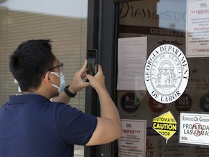 caption: A man copies phone numbers posted on the locked doors of a Georgia Department of Labor office in in Norcross, Ga. Millennials are facing the second — or even third — economic downturn of their adult lives.