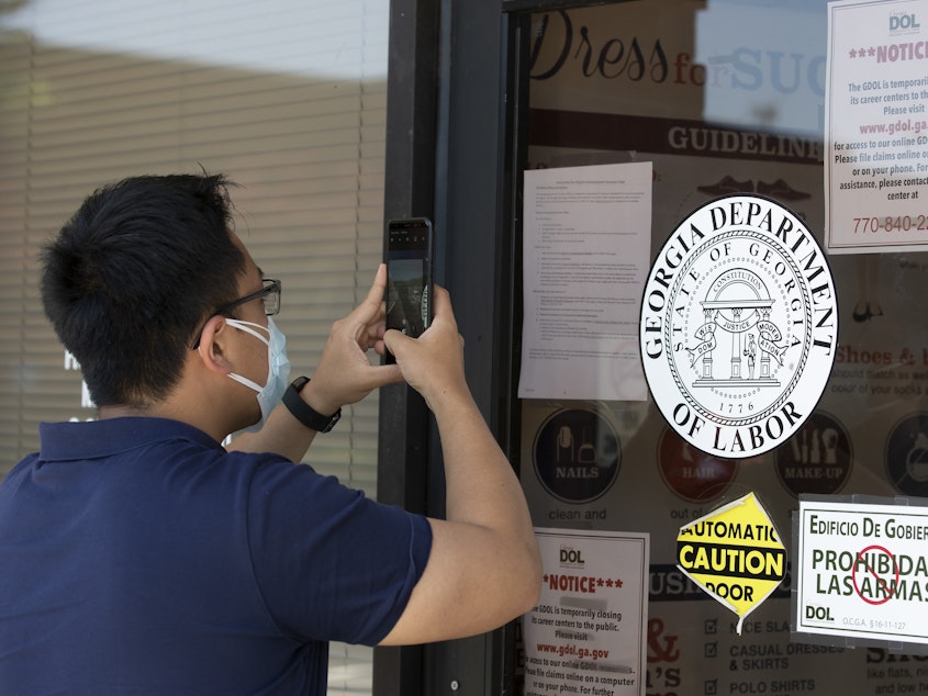 caption: A man copies phone numbers posted on the locked doors of a Georgia Department of Labor office in in Norcross, Ga. Millennials are facing the second — or even third — economic downturn of their adult lives.