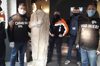 caption: Carabinieri (Italian paramilitary police) officers of the art squad's archaeological unit pose with a headless Roman statue wearing a draped toga in Brussels on Wednesday, Feb. 3, 2021.