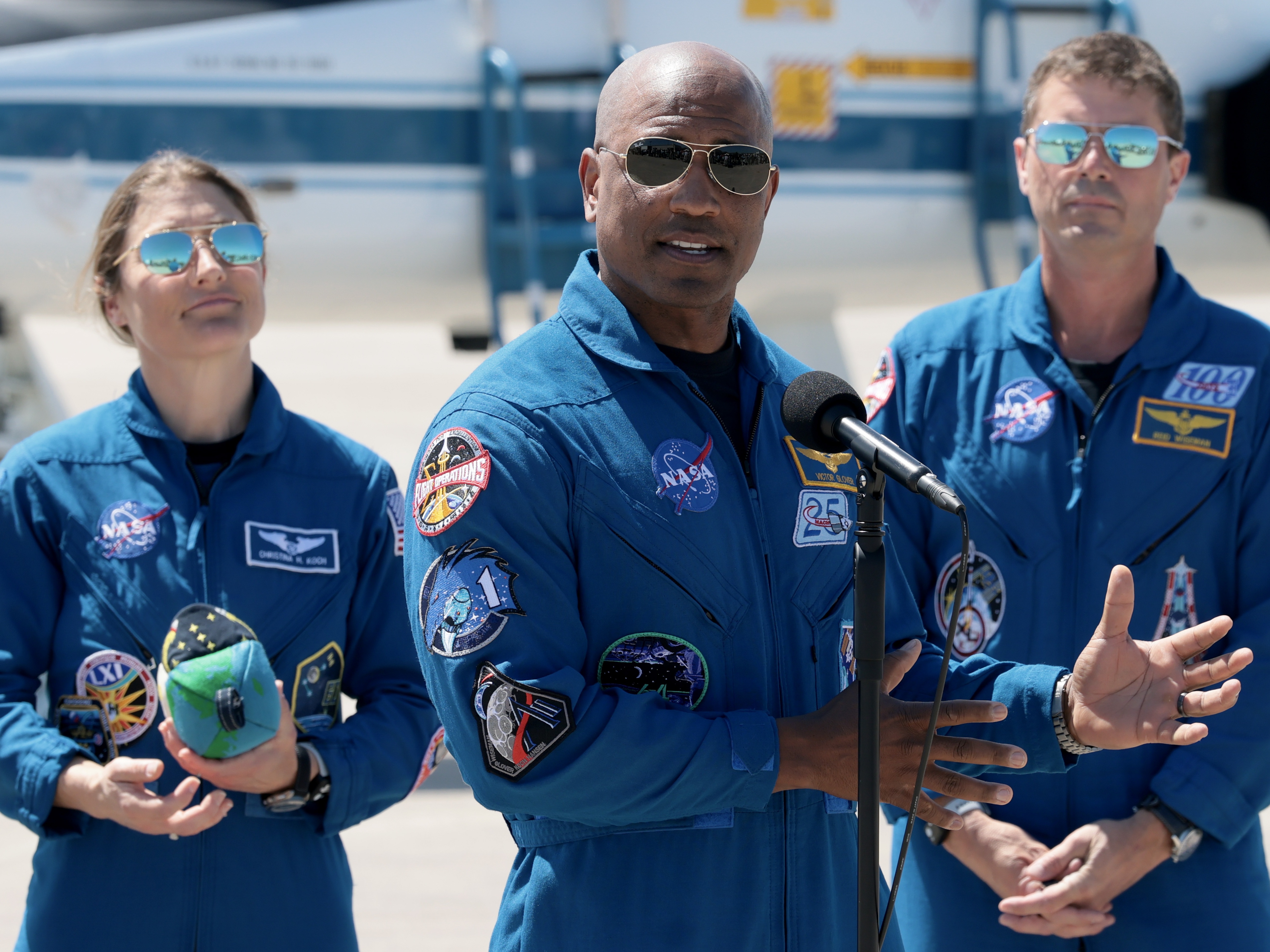 caption: Artemis II crew members — mission specialist Christina Koch (left) and commander Reid Wiseman (right) — listen as pilot Victor Glover speaks to the media after arriving at the Kennedy Space Center on March 27, 2026 in Cape Canaveral, Florida. The astronauts' planned 10-day mission will take them around the Moon and back to Earth.